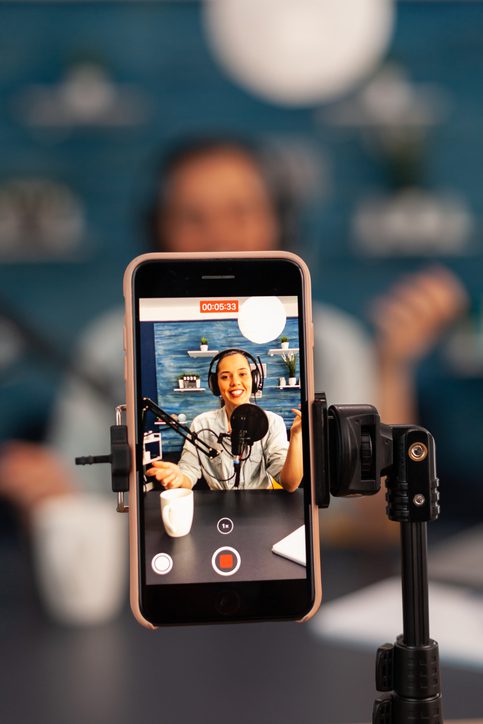 Close up of influencer vlogger record live broadcast looking at smartphone on tripod at home studio podcast. Creative content creator making online video for subscribers audience