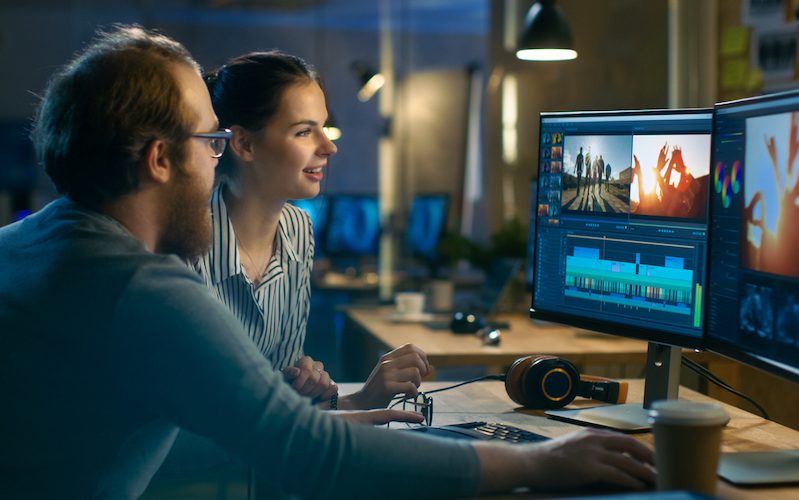 Beautiful Female and Handsome Male Video Editors Discuss Footage They're Working On. They Enjoy Working Together in a Cozy Creative Studio.